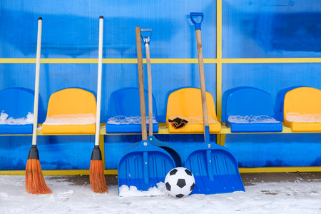 Snow-covered substitute bench, tools for clearing snow and classic soccer ball on winter stadium outdoorの写真素材