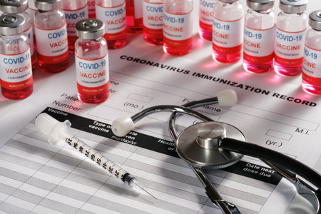 Stethoscope, syringe and vaccine vial glass bottles on background for vaccination against COVID-19 SARS-CoV-2 coronavirus pandemic lying on immunization document.の写真素材