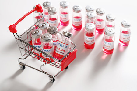 Wire shopping cart with vaccine vials bottles for vaccination against COVID-19 SARS-CoV-2 coronavirus pandemic on white backgroundの写真素材