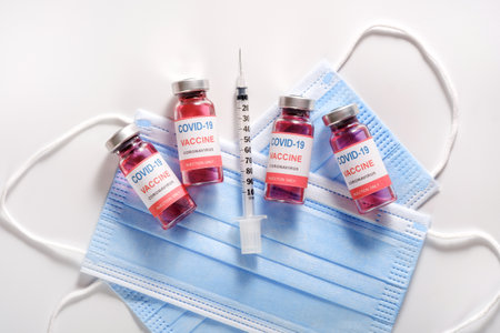 Glass vaccine vials and syringe for vaccination against the   pandemic lying on surgical protective masks, flat layの写真素材