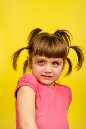 Portrait of crying little caucasian girl with pigtails and bruise under the eye on yellow background. Vertical orientationの写真素材