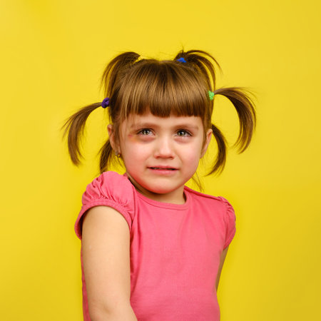 Portrait of crying little caucasian girl with pigtails and bruise under the eye on yellow background.の写真素材