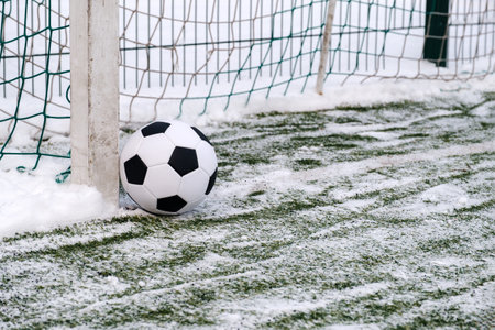 Soccer ball placed on snowy grass near goal in winter on sports groundの写真素材
