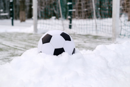 Soccer ball placed on snowdrift near goal in winter on sports groundの写真素材