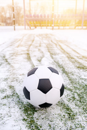Soccer ball placed on snowy grass in winter on sports ground and tribune on background, copy space, vertical orientationの写真素材