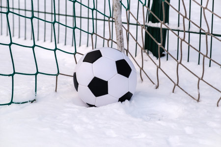 Soccer ball placed on snowy grass in corner of football goal in winter on sports groundの写真素材