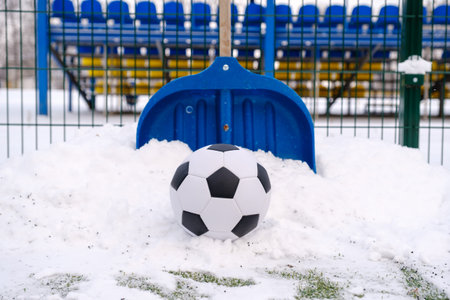 Classic soccer ball, snow-covered football field and shovel on winter stadium outdoor