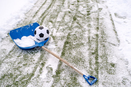 Classic soccer ball placed in shovel on snowy artificial grass of soccer field on winter stadiumの写真素材