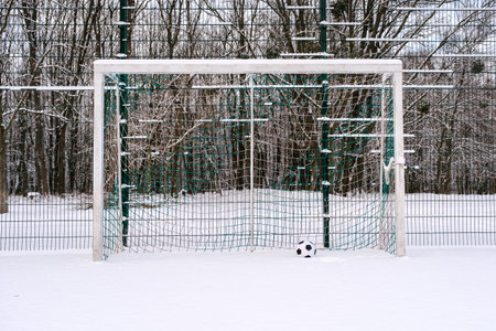 Soccer ball placed in goal on snowy sports ground in winterの写真素材