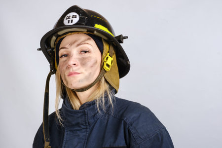 Close up face of young brave woman in uniform, hardhat of firefighter looking at camera isolated on...
