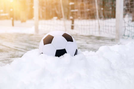 Soccer ball placed on snowdrift near goal in winter on sports ground, sunny dayの写真素材