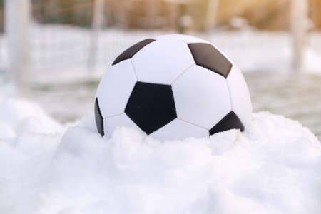 Soccer ball placed on snowdrift near goal in winter on synthetic sports ground at sunny dayの写真素材