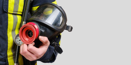 Full protective breathing mask in hand of unrecognized firefighter, rescue and fire fighter equipment isolated on gray background, copy spaceの写真素材