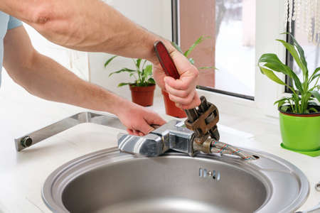 Plumber hands removes the old faucet from the kitchen sink with an adjustable wrench to replace it with a new oneの写真素材