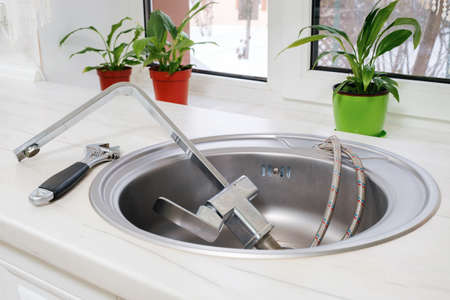 Removed old kitchen faucet in sink and tools to replace it on kitchen countertopの写真素材