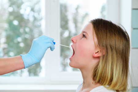 Female doctors hand in medical glove with a cotton swab takes an analysis from the mouth of young...
