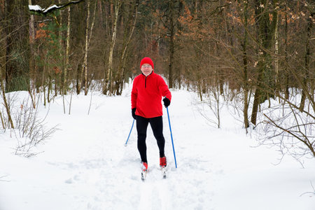 Elderly smiling caucasian man goes cross-country skiing in the winter in the snowy forestの写真素材