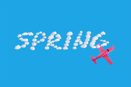 Pink airplane goes into a sharp turn on blue background and word spring of abstract shapes of cloud....