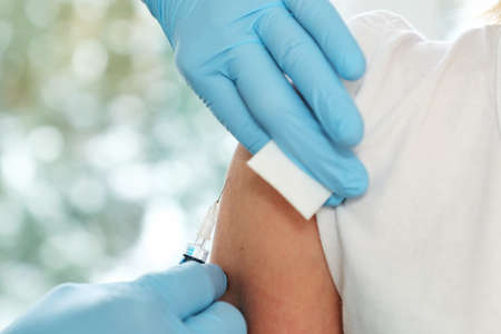 Doctor hands in protective gloves making vaccination in the shoulder of patient close-up. Vaccination against COVID19の写真素材
