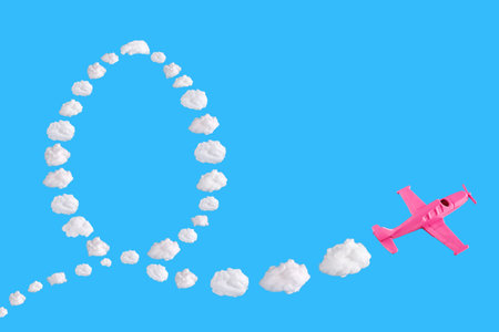 Pink airplane goes into a sharp turn on blue background and easter egg of abstract shapes of cloud. Festive minimal composition. Happy easter holiday concept, copy spaceの写真素材