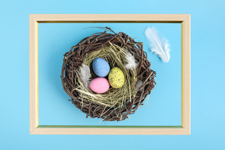 Wooden frame on blue background with painted easter egg nest flat lay. Minimal abstract easter holiday concept background.の写真素材