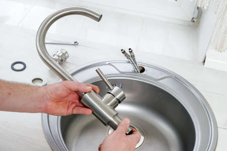 Close-up plumber hands holds a new faucet for installing into the kitchen sink, plumbing work or renovationの写真素材