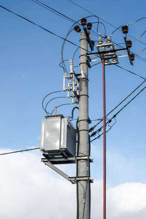 High voltage transformer mounted on a pole on blue sky background at sunny day. Vertical orientationの写真素材