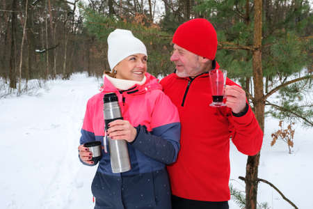 Happy smiling elderly caucasian couple drink warm drinks at winter parkの写真素材