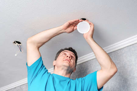 Middle aged caucasian electrician is installing LED spotlights in hole on the plasterboard ceiling. Closeup viewの写真素材