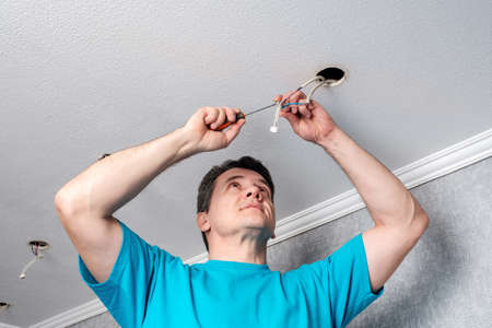 Middle aged caucasian electrician prepare cables before installing LED spotlights on the ceiling.の写真素材