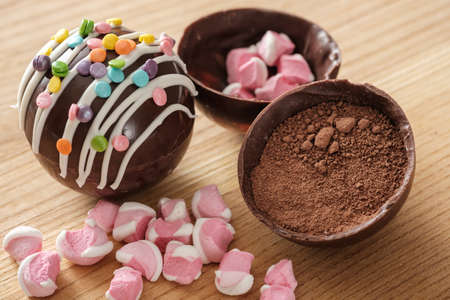 Cocoa bombs are black chocolate shells filled with cocoa powder and marshmallows that melt when hot milk is added, open in a mug and create a trendy delicious drink. Closeup view, selective focusの写真素材