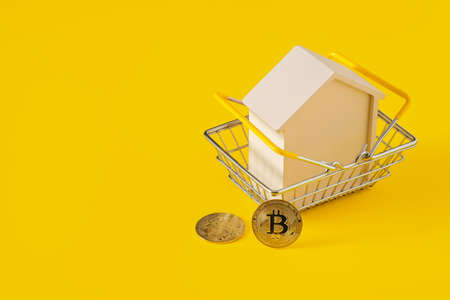 Wooden house in a shopping basket and bitcoins on yellow background. E-commerce concept, copy space for textの写真素材