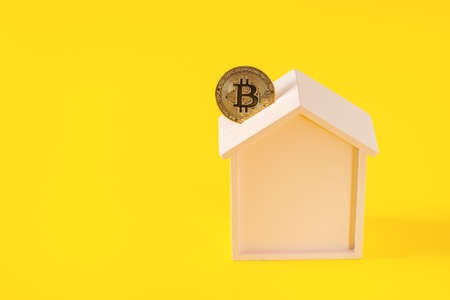 Wooden house moneybox and bitcoin on yellow background. E-commerce concept, purchase of real estate for cryptocurrency concept, copy space for textの写真素材