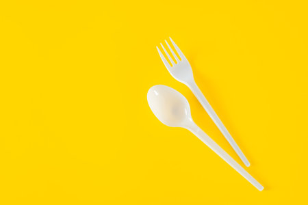 Plastic spoon and fork on yellow background. Picnic table setting, plastic disposable tableware, copy spaceの写真素材