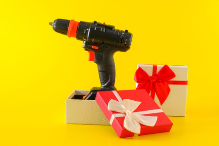 Handheld cordless power drill, hand battery screwdriver in gift box on yellow background. Concept of...