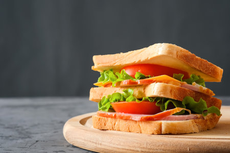 Tasty sandwich with ham, salad, cheese and tomatoes on gray background, selective focus, close-up viewの写真素材