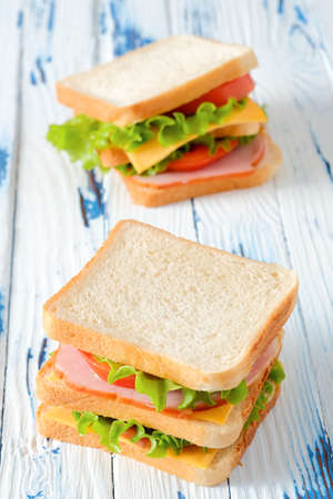 Two tasty sandwiches with ham, salad, cheese and tomatoes on rustic wooden table, selective focus, close-up view, vertical orientationの写真素材