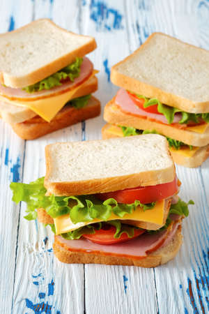 Three tasty sandwiches with ham, salad, cheese and tomatoes on rustic wooden table, selective focus, close-up view, vertical orientationの写真素材