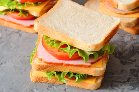 Tasty sandwiches with ham, salad, cheese and tomatoes on gray background, selective focus, close-up viewの写真素材