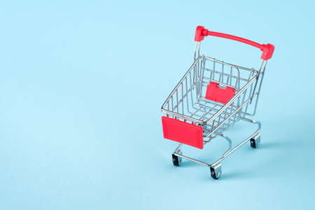 Empty red shopping cart on blue background, mini metal cart isolated on yellow background, copy space for textの写真素材