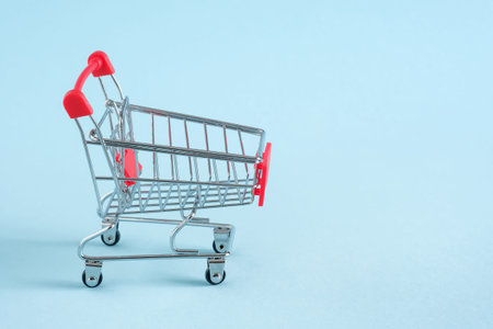 Empty red shopping cart on blue background, mini metal cart isolated on yellow background, copy...