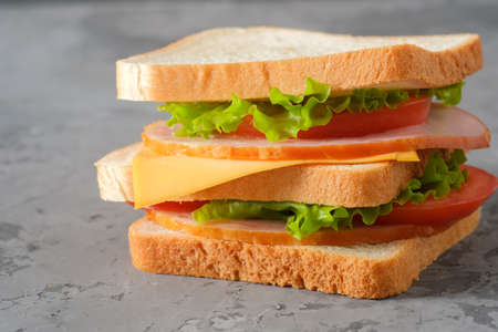 Tasty sandwich with ham, salad, cheese and tomatoes on gray background, selective focus, close-up viewの写真素材