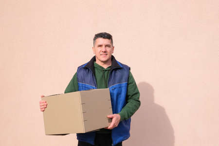 Middle-aged delivery man in uniform holding and carrying a cardbox on pink wall background. Volunteer delivery of food or medicine during the  pandemicの写真素材