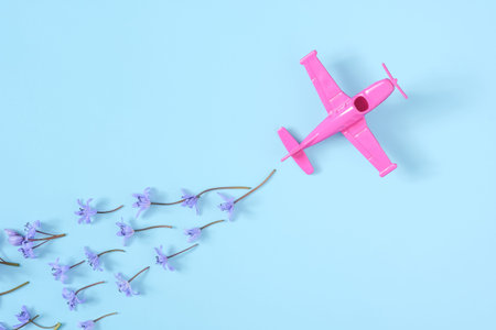 Pink airplane takes into a sharp turn on blue background with trail of spring snowdrop flowers. Minimal composition. Transportation, travel or vacation concept, copy space for textの写真素材