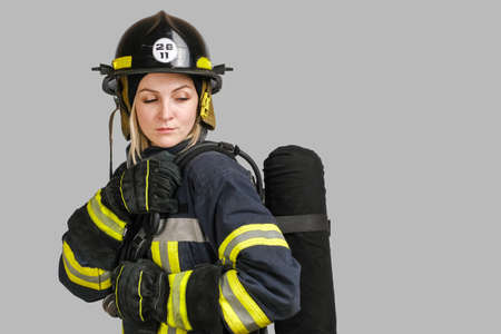 Young caucasian woman in uniform of firefighter posing in profile with Air tank on her back isolated on gray background, copy spaceの写真素材