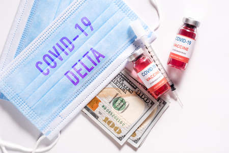 Top view of new coronavirus infection vaccine against COVID-19 Delta variant strain with dollar bills and clean medical mask on white backgroundの写真素材