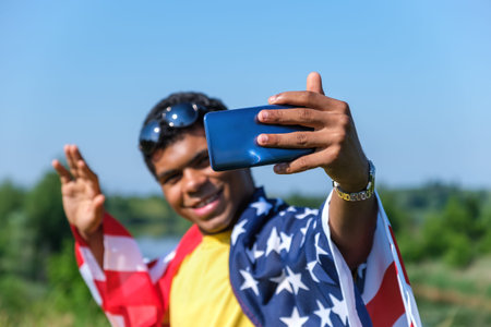 Close-up hand with smartphone of cheerful smiling African American young man in sunglasses and...