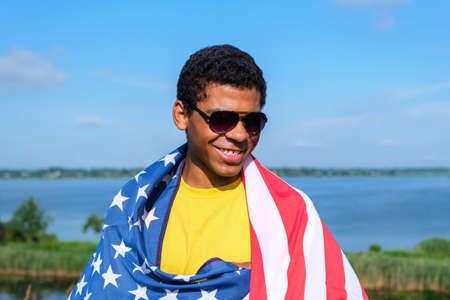 Young smiling Afro American sportsman holds soccer ball and showing his arm after receiving a vaccine at sunset in summerの写真素材