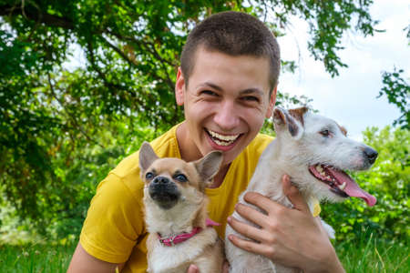 Young caucasian man hugs two dogs Jack Russell and a chihuahua and laughs cheerfully in the summer parkの写真素材