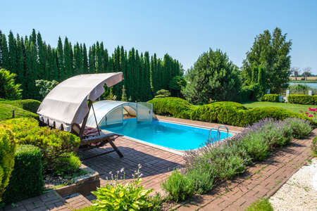 Swimming pool and garden with nicely trimmed bushes and garden swing in backyard. Landscape design. High quality photoの写真素材